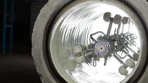 Roboter mit Rollen in einem runden, hell erleuchteten Rohr, auf glattem Betonboden platziert.